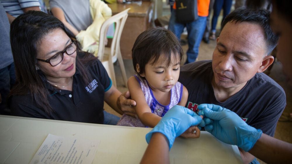 A Palawan local man, right, comforts his daughter, center, while ENSURE project's stakeholder councillor Nomena Saibodin looks on as a RITM staff takes blood sample for the malaria test in Rizal, Palawan, Philippines, Tuesday, March 14, 2017. (Joshua Paul for LSHTM)