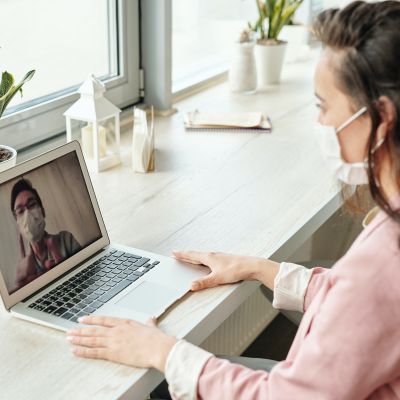 Two people in medical masks videoconferencing.