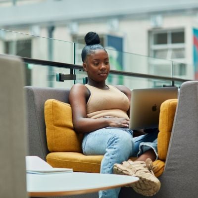 Female student sitting on a sofa, working on a laptop.