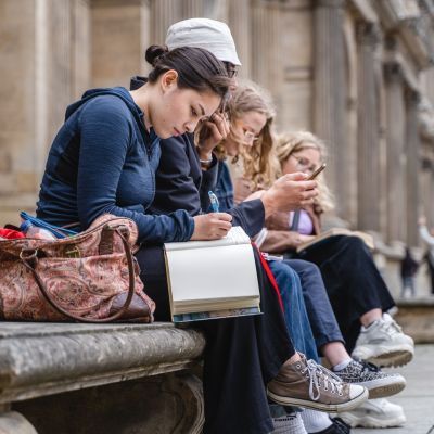Group of students sitting on a wall with books