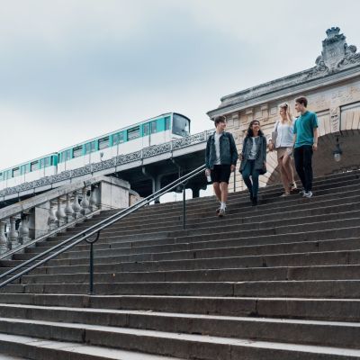 Four students walking down steps in Paris, with metro train in the background