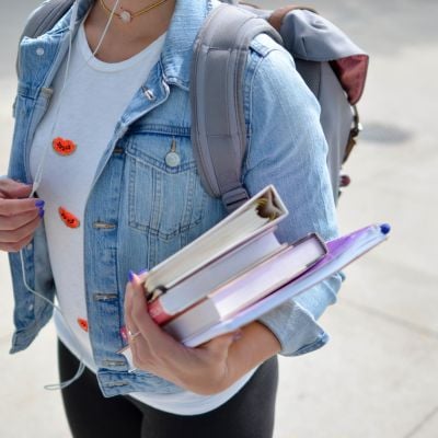Female student in blue denim jacket holding books and folders.