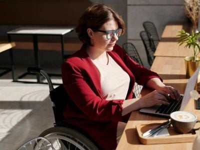 Woman in red, sitting in a wheelchair accessing learning materials via a laptop. Credit: Photo by Marcus Aurelius: https://www.pexels.com/photo/woman-in-red-blazer-sitting-on-wheelchair-4063590/