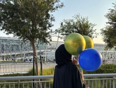 Tehmina holding 3 balloons looking onto a building on a sunny day