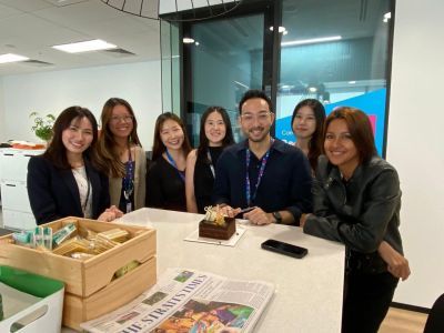 Adelia Koh with a team of smiling colleagues gathered around a table.