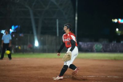 Adelia Koh pitching during a softball match at night.