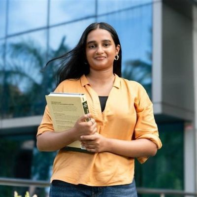 Tharushi Jayathunga wearing a yellow blouse holding books outside an academic building.