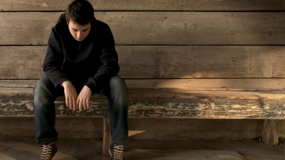 A young person sitting solemnly on a wooden bench